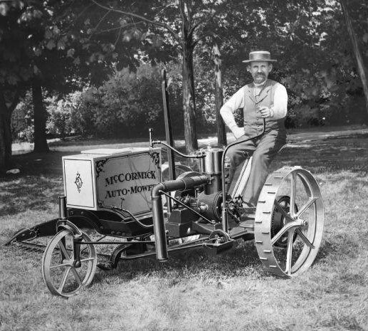 A man poses atop his McCormick Auto-Mower with his left hand on the steer, and his right hand on his hip.