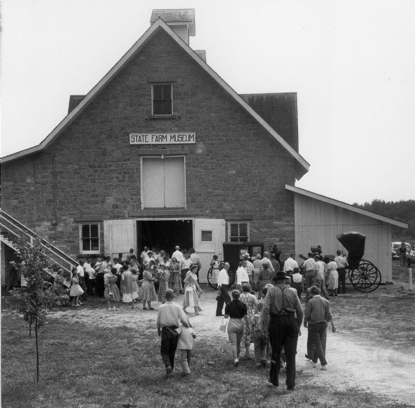 A large building with a sign that reads "State Farm Museum" and doors open for a crowd of people visiting the museum.