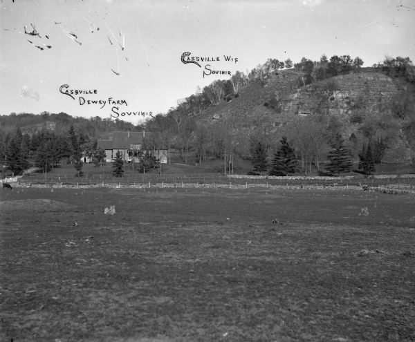 A large clear field with a house in the distance. The image has writing that reads "Cassvile Dewey Farm Souvinir," and "Cassville WI. Sovinir"